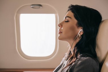 Çekici bir iş kadınının yan görüntüsü. Gözleri kapalı. Özel jette müzik dinliyor. 