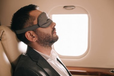 Özel jette oturan uyku maskeli iş adamının yan görüntüsü 