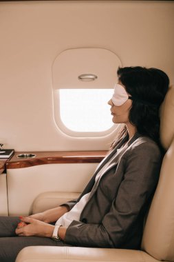 Özel jetteki uçak penceresinin yanında oturan uyku maskeli iş adamının yan görüntüsü 