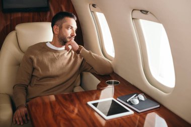 handsome bearded man looking at airplane window in first class of private jet  clipart
