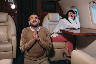 Uçakta korkmuş bir kadının yanında dua eden bir adamın seçici odağı. 