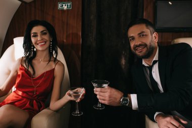 Kırmızı elbiseli mutlu adam ve kadın özel jetlerinde martini bardakları tutuyorlar. 