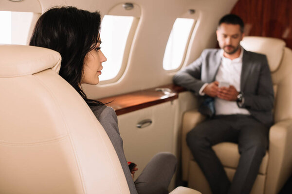 selective focus of attractive businesswoman in private jet with businessman 