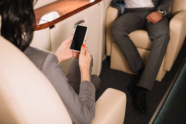 cropped view of businesswoman holding smartphone with blank screen near businessman in private jet 