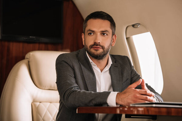 selective focus of handsome businessman sitting with clenched hands in private jet 