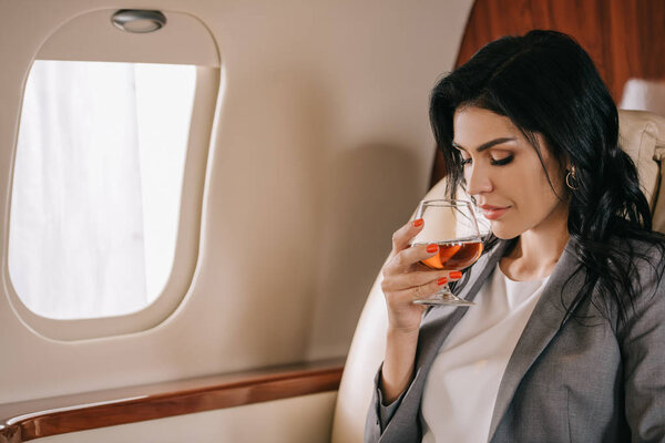 attractive businesswoman holding glass with cognac in private jet 