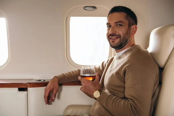 坐在头等舱的私人飞机上 快乐的男人拿着酒杯喝着白兰地 — 图库照片