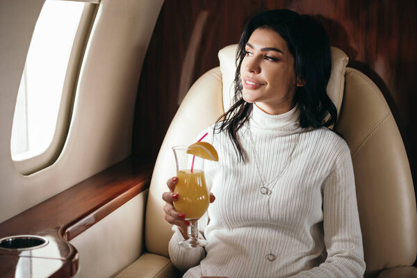 happy woman holding tasty cocktail in private jet 