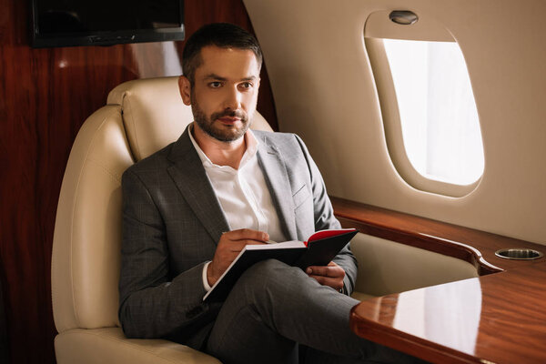 selective focus of bearded businessman holding notebook and pen in private jet 