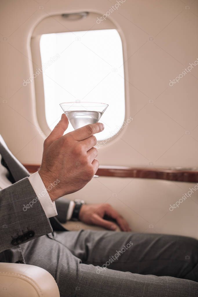 cropped view of businessman holding martini glass with drink in private jet 