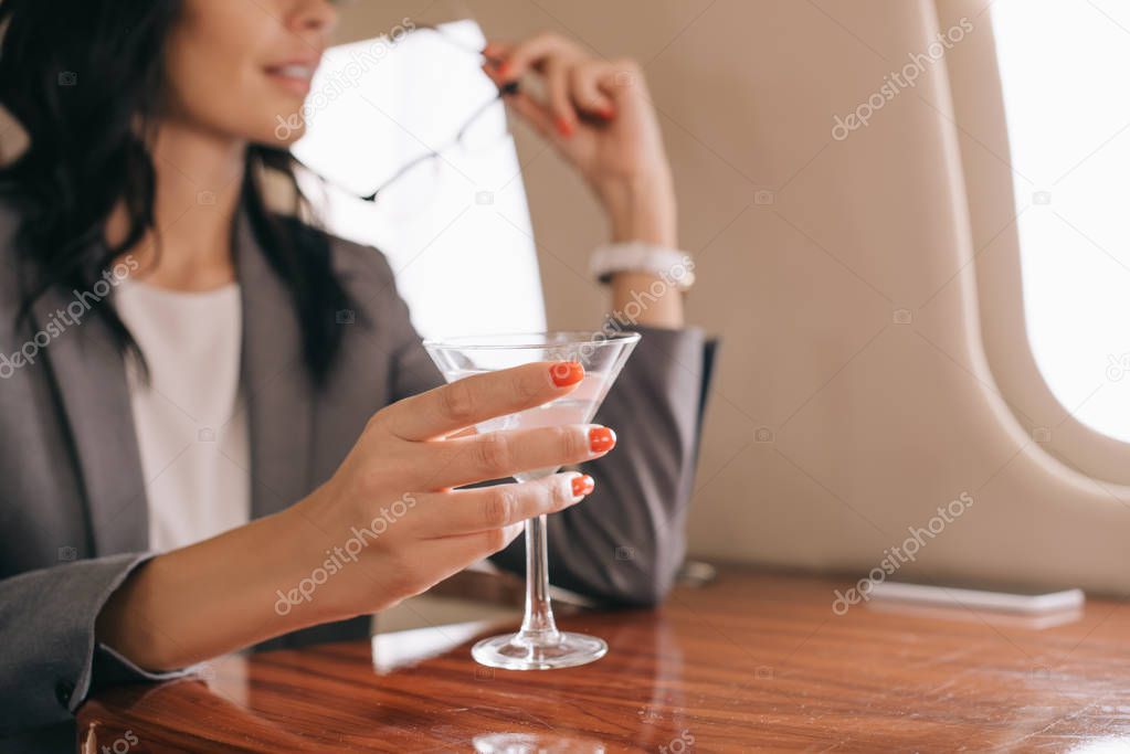 cropped view of businesswoman holding martini glass in private jet 