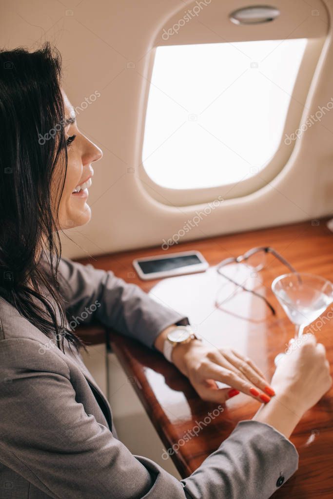 selective focus of cheerful businesswoman holding martini glass in private jet 