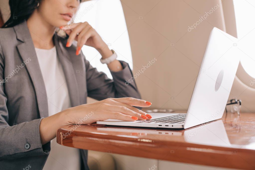 cropped view of businesswoman using laptop in private jet 