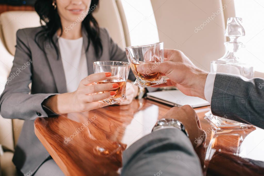 cropped view of businessman and businesswoman toasting glasses with alcohol in private jet 