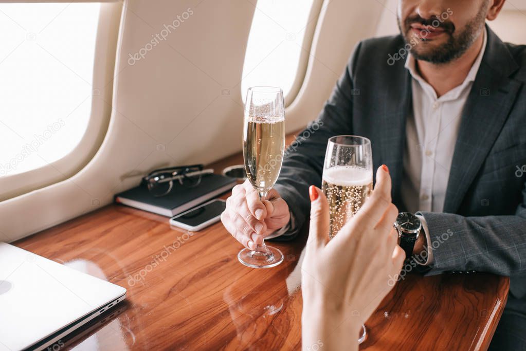 cropped view of woman and bearded man holding champagne glasses in private jet 