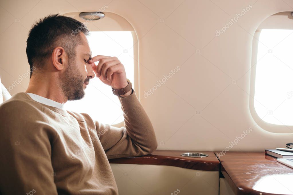tired bearded man with closed eyes sitting in private jet 