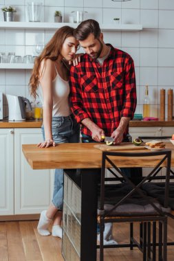 Yakışıklı erkek arkadaşının omzuna yaslanan çekici kız taze avokado kesiyor.