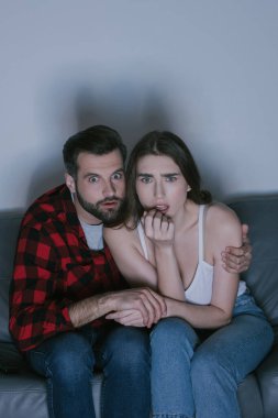 Evde birlikte film izlerken el ele tutuşan korkmuş çift.