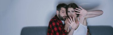 Kollarını uzatmış korkmuş kız korkmuş erkek arkadaşının yanında film izliyor, yatay görüntü.