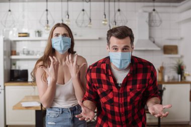 irritated couple in medical masks screaming and gesturing while looking at camera clipart