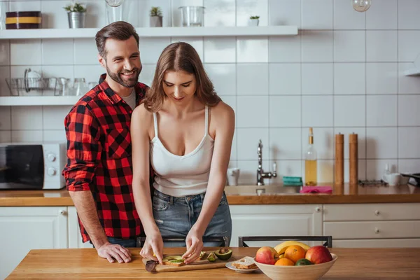 Glad Man Tittar Kameran Nära Attraktiv Flickvän Förbereder Frukost Med — Stockfoto