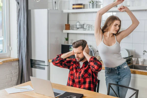 Cheerful Girl Dancing Boyfriend Covering Ears Hands While Sitting Laptop — Stock Photo, Image