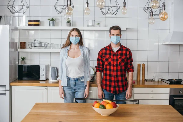 Jovem Casal Máscaras Médicas Olhando Para Câmera Enquanto Cozinha Moderna — Fotografia de Stock