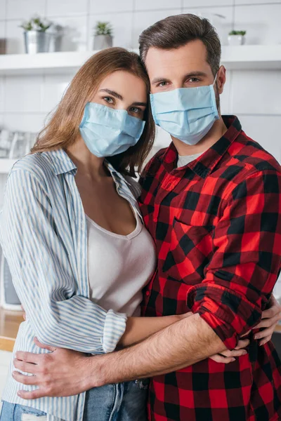 Pareja Joven Máscaras Médicas Abrazando Mirando Cámara Cocina —  Fotos de Stock