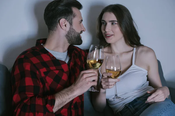 幸せな若いカップルがソファに座って白ワインのグラスを持ちながらお互いを見て — ストック写真