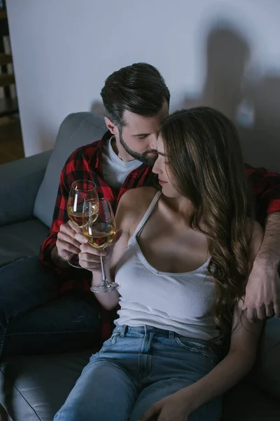 幸せそうな若いカップルが白ワインのグラスを片手にソファに座り — ストック写真