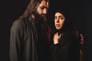Muslim woman in hijab looking at camera near husband isolated on black  clipart