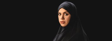 Panoramic shot of muslim woman in hijab looking at camera isolated on black  clipart