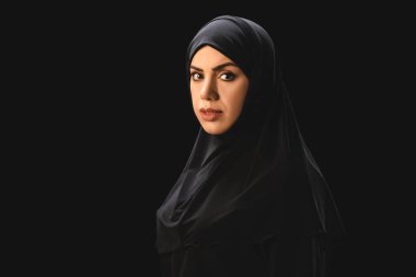 Side view of beautiful muslim woman looking at camera isolated on black  clipart