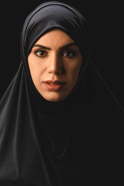 Portrait of beautiful muslim woman in traditional hijab looking at camera isolated on black  clipart