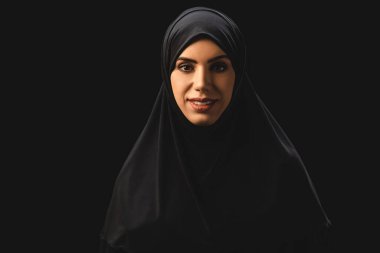 Beautiful muslim woman smiling at camera isolated on black  clipart