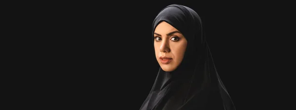 Panoramic shot of muslim woman in hijab looking at camera isolated on black