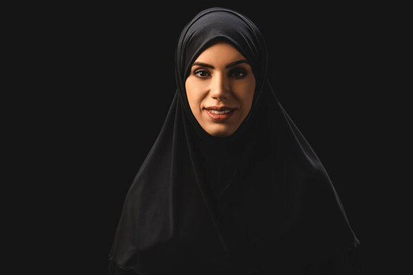 Beautiful muslim woman smiling at camera isolated on black 