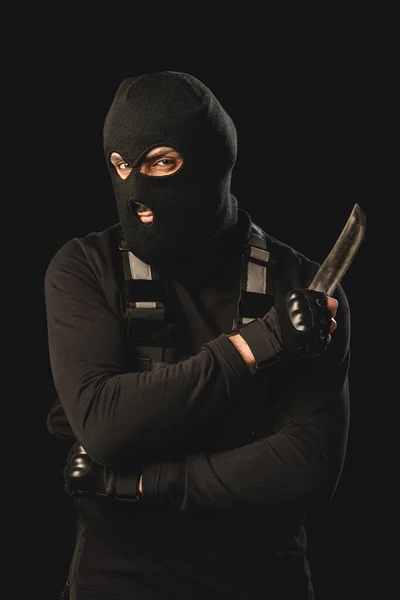 Muslim terrorist in balaclava holding dagger and looking at camera isolated on black