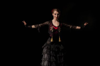 Çekici bir kadın, uzanmış elleriyle siyah üzerinde Flamenko dansı yapıyor.