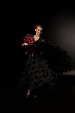 Genç flamenko dansçısı elinde yelpaze ve siyah üzerinde dans ediyor 