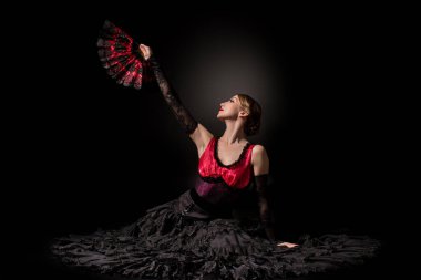 Mutlu ve genç flamenko dansçısı siyahların üzerinde dans ederken yelpaze tutuyor 