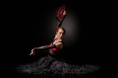 Genç flamenko dansçısı siyahın üzerinde otururken yelpaze tutuyor