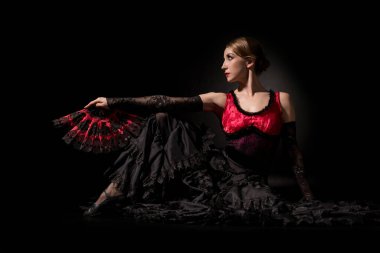 Zarif flamenko dansçısı yelpaze tutuyor ve siyah üzerine oturuyor.