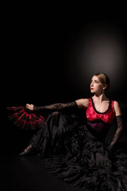 Güzel flamenko dansçısı yelpaze tutuyor ve siyah üzerine oturuyor.