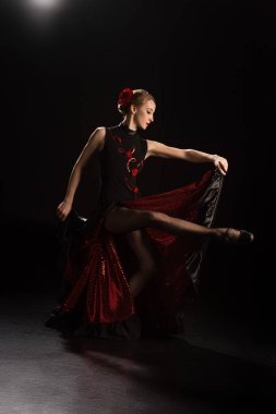 side view of young woman touching dress and dancing flamenco on black  clipart