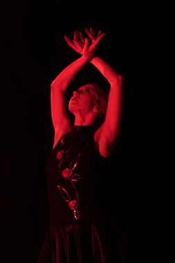 Kafasının üstünde elleri olan genç bir kadına kırmızı ışık. Siyah üzerinde yalnız dans eden flamenko.  