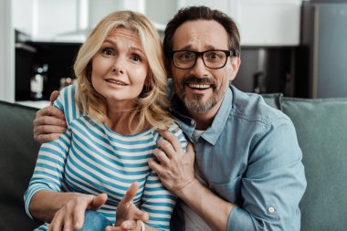 Evde televizyon izlerken karısını kucaklayan korkak bir adam. 