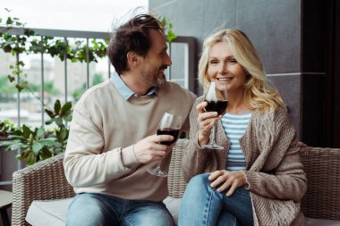 Yakışıklı olgun adam terasta bir bardak şarapla gülümseyen karısına bakıyor. 