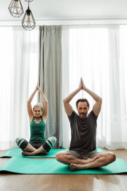 Oturma odasındaki spor minderleri üzerinde yoga yapan olgun bir çift.
