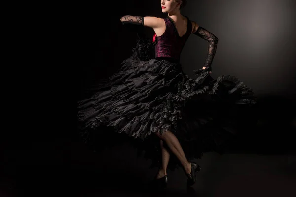 cropped view of flamenco dancer in dress and shoes dancing on black
